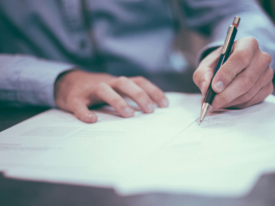 photograph of a person's hands holding a pen and reviewing paperwork